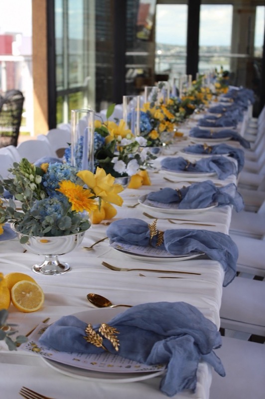 A waterfront banquet table styled with blue hydrangea, yellow roses and gold details